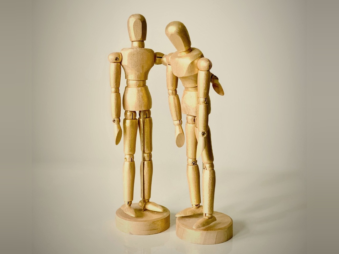 Two wooden artist figures standing together, one resting a hand on the other's shoulder